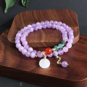 Detalle de una pulsera de piedras púrpuras de varias vueltas con un dije de jade blanco