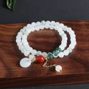 Detalle de una pulsera de jade blanco de doble hilo con ágata roja y dije de hebilla de la paz.