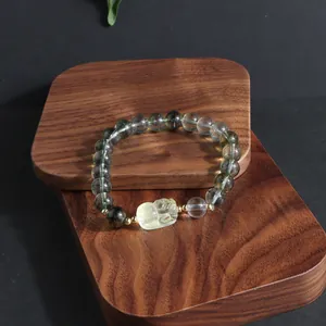 Detailed view of green ghost crystal bracelet with a carved yellow lion charm on wood