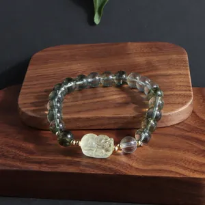 Close-up of Green Ghost and yellow crystal bracelet with carved lion centerpiece on wood.