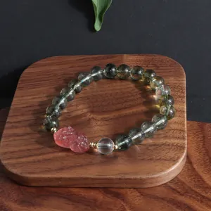 Close-up of green ghost crystal bracelet with a pink carved lion charm on wood