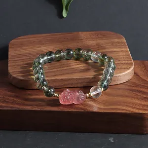 Close-up detail of green ghost crystal beads and pink carved lion charm on a wooden stand