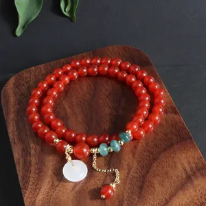 Detalle de pulsera multihilo de piedra natural roja con colgante de jade blanco