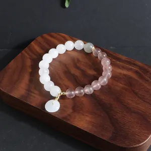 Nahaufnahme eines chinesischen Perlenarmbands mit weißer Jade und rosa Achat auf Holz.