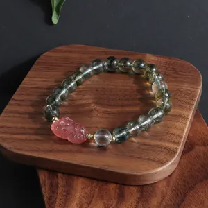 Close-up of a green phantom quartz crystal bracelet with a pink lion charm on wood
