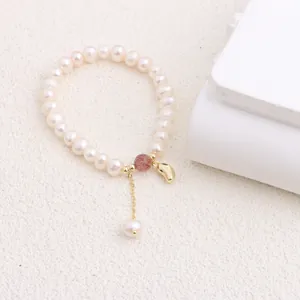 Detailed view of elegant natural freshwater pearl bracelet with gold tassel and red bead.