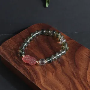 Close-up detail of a handmade green ghost crystal bead bracelet with a pink carved lion charm.