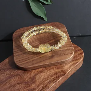 Macro detail of a natural yellow citrine bracelet with a carved pixiu charm on wood.