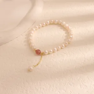 Close-up of freshwater pearl bracelet featuring a strawberry quartz bead and gold dangle