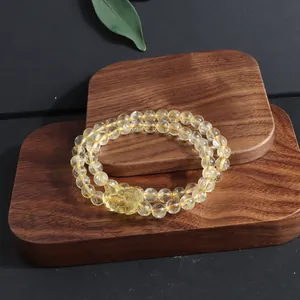 Detail of double-strand lemon quartz bracelet with carved Pixiu charm on wood.
