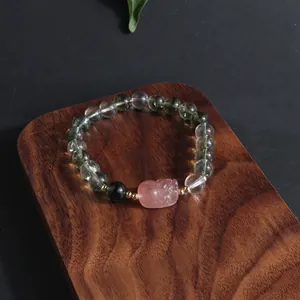 Close-up of Green Phantom Quartz bracelet with pink carved lion bead on wooden tray