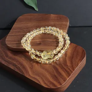Detail view of a natural citrine bead bracelet with a carved pixiu charm on wood.