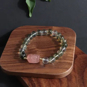 New Chinese style green phantom quartz bracelet with pink carved lion bead on wood tray.