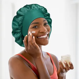 Woman wearing a dark green satin bonnet while applying cream for beauty routine