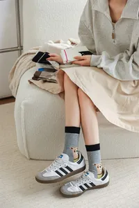 Gros plan d'une femme portant des chaussettes grises avec motif ours et des baskets blanches.