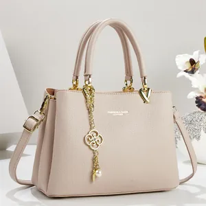 Detailed view of a pinkish-beige leather handbag with an elegant gold floral pearl pendant.