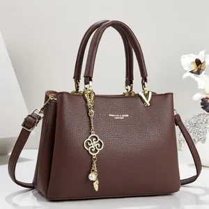Detail view of brown textured leather handbag with elegant gold flower pendant