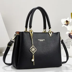 Detailed view of a black pebbled leather handbag with gold-tone clover charm and pearl.