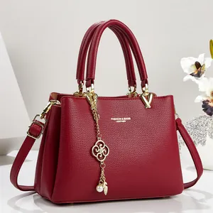 Detailed view of an elegant burgundy leather handbag featuring gold hardware and a pearl charm