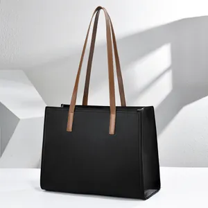 Vista lateral de un bolso tote negro para portátil en cuero granulado con asas marrones