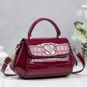 Detalle de elegante bolso burdeos con estampado de cocodrilo y cierre de flor dorada