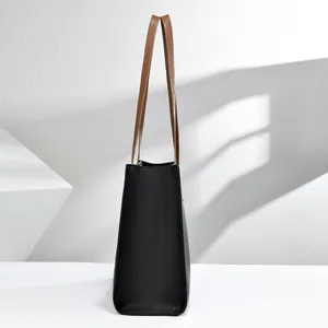 Vista lateral de un bolso tote de cuero granulado negro con asas marrones y espacioso