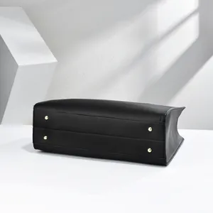 Detailed bottom view of a black leather tote bag with four golden protective studs.