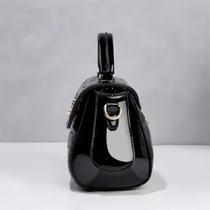 Vista lateral de elegante bolso de mano en charol negro con motivo de piedra en relieve.
