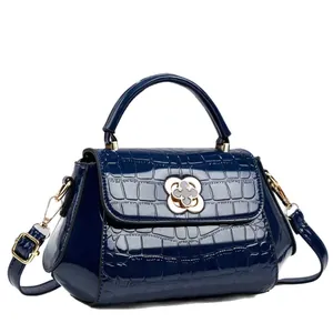 Elegante bolso de charol azul oscuro con estampado de cocodrilo y cierre de flor dorada.