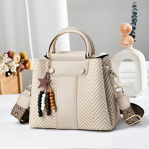 Elegante bolso de mano beige con estampado tejido, colgante estrella y asa dorada.