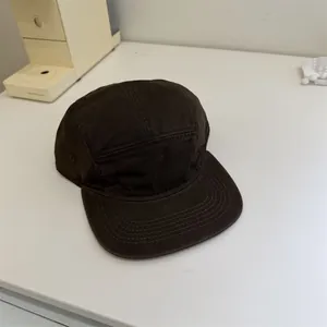 Casquette de baseball rétro marron foncé à 5 panneaux à bord court dans un décor minimaliste