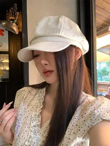 Side profile of a woman wearing a vintage white checked baker boy hat in a cafe setting