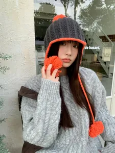 Asian model wearing a grey and orange knitted pom-pom beanie with ear flaps