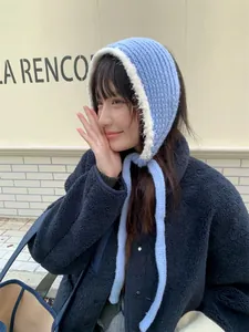Close-up of a blue knitted earmuff bonnet with fuzzy white trim worn by a model