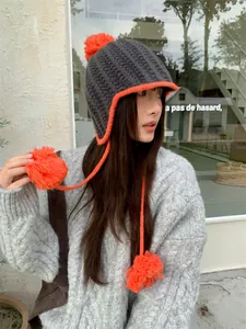 Close-up detail of a stylish grey and orange knitted pom-pom beanie with ear flaps