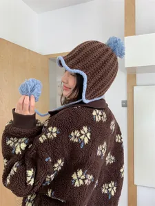 Detail view of brown knit hat with blue pom-poms and matching fleece jacket