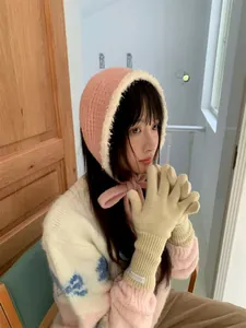Detailed shot of a pink knitted plush ear cover with bow and warm beige winter gloves