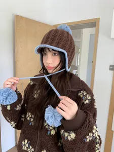 Detail of a brown knit hat with light blue pom-poms and ear flaps on a model