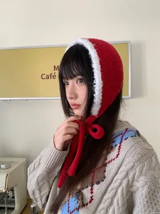 Red knitted tie balaclava with white fuzzy trim worn by model in a café setting