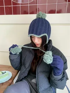 Asian woman wearing a stylish navy and mint green knit beanie with pom-poms and ear flaps