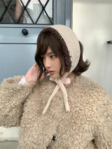 Close-up detail of beige knitted ear muffs with brown plush trim and tie closure