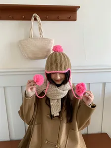 Model wearing cute knitted beanie with pink pompoms and earflaps in a cozy setting