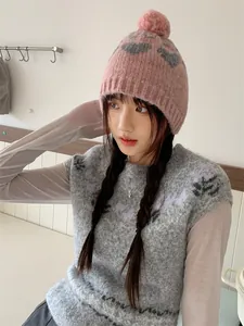 Close-up of a cute pink knitted beanie with a pom-pom and grey heart patterns on a model