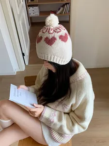 Detail view of a vintage cream knit beanie with red heart patterns and pom-pom