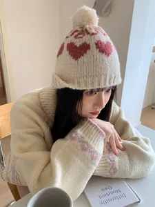 Close-up of a cozy knitted beanie featuring pink heart patterns and a soft pom-pom detail.