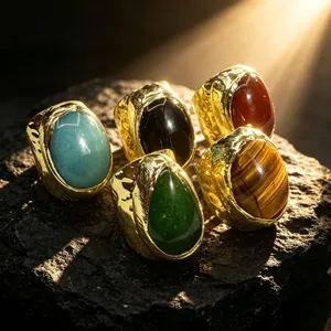 Detailaufnahme goldener Breitbandringe mit bunten Edelsteinen auf dunklem Naturstein.