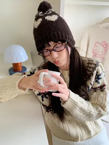 Close-up of vintage heart-patterned knit beanie with brown pom pom on model