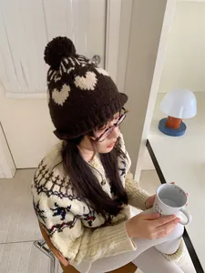 Side view of a vintage knit beanie with heart patterns and a pom-pom