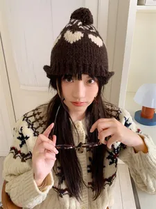 Detailed view of a vintage knitted beanie with white heart patterns and a brown pom-pom