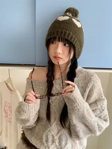 Detailed view of model wearing a dark green retro knit beanie with heart pattern and pom-pom.